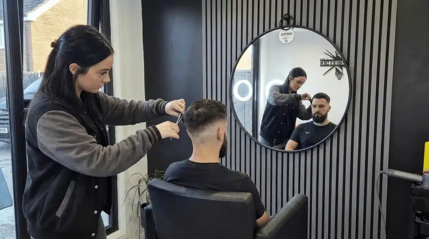 Barber cutting a male client's hair in The Barbers Den, Millisle, with a round mirror reflecting the scene in the background